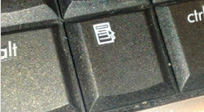 A photograph of a computer keyboard.  The Alt key is on the left. The Ctrl key is on the right. A Program key, showing a mouse pointing at a drop-down menu is in the middle. Not all computers have this key. Shift+F10 is the awkward replacement when the key is missing.